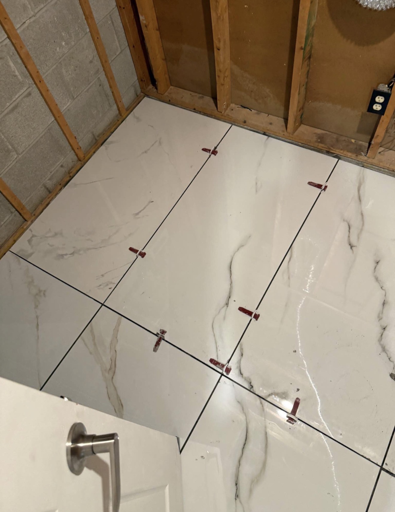 Marble-patterned floor tiles being laid with levelling spacers in a room under renovation