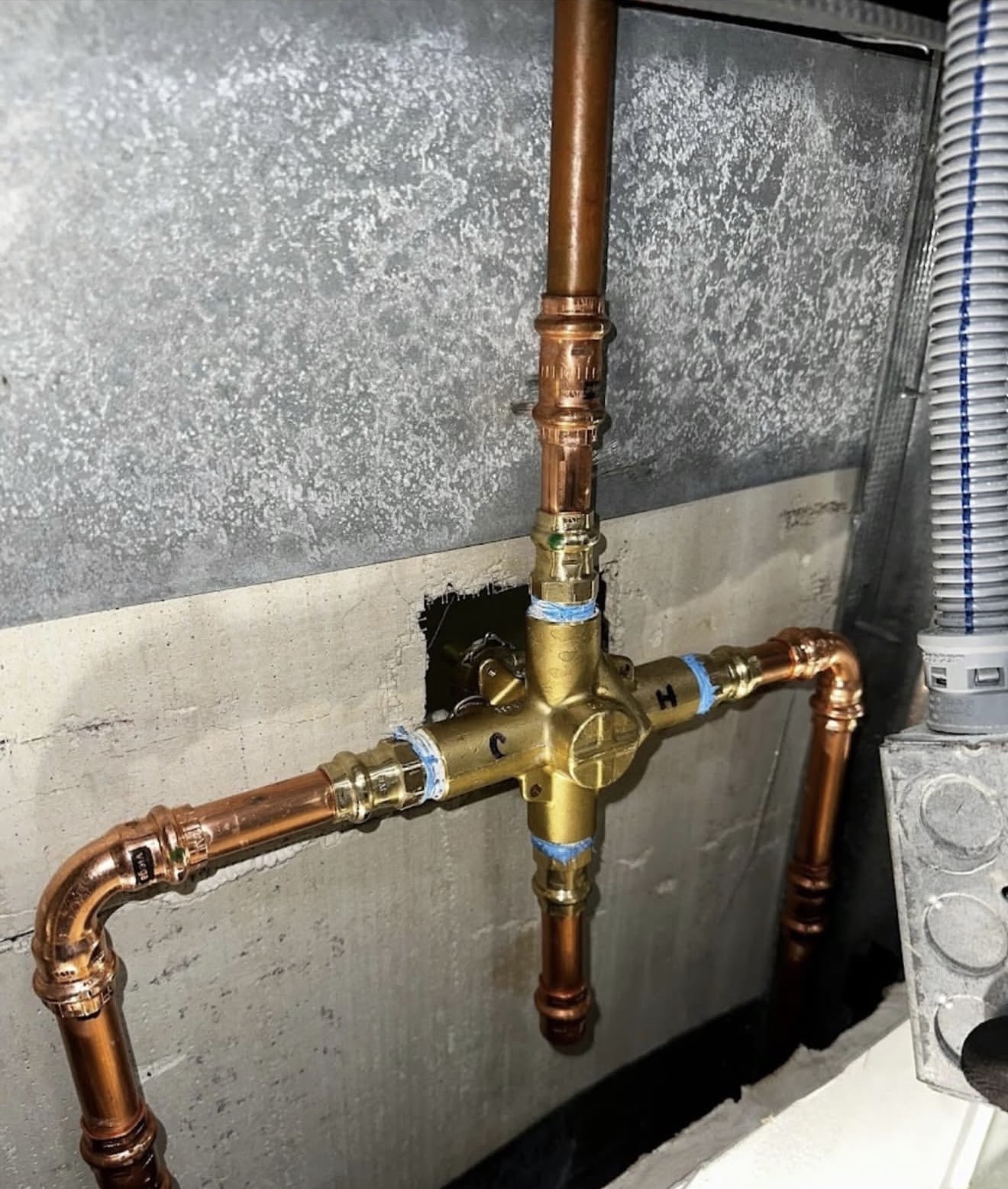 Brass four-way mixing valve connected to copper piping with press-fit connectors inside a wall cavity